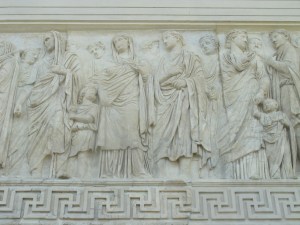 Agrippa (head covered by a fold of his toga) leads the Imperial household. The child tugging on his toga may be one of his sons (and heir to Augustus, as his mother was Julia, Augustus' sole biological child). The woman directly after is thought to be Julia, or perhaps Livia, Augusts' empress.